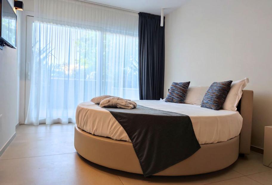 Camera moderna con letto rotondo e grandi finestre con tende bianche.
